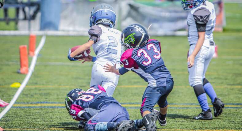 two-youth-pop-warner-football-players-kids-tackling-a-child-running-with-the-ball
