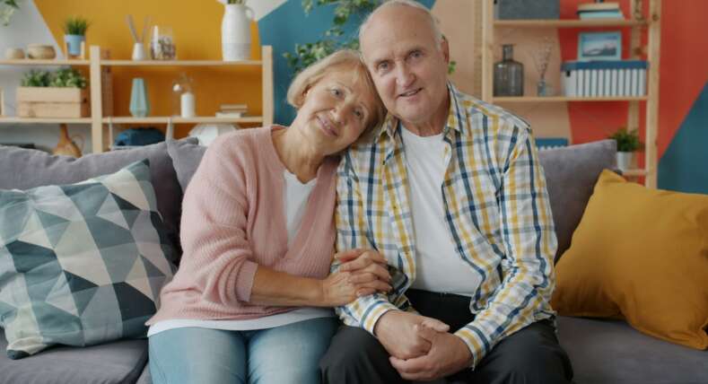 two-senior-citizen's-holding-hands-on-the-couch